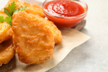 Tasty fried chicken nuggets on light grey table, closeup