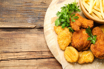Tasty nuggets and deep fried chicken pieces with garnish on wooden table, top view. Space for text