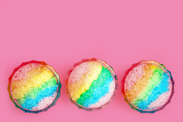 Rainbow shaving ice in glass dessert bowls on pink background, flat lay. Space for text