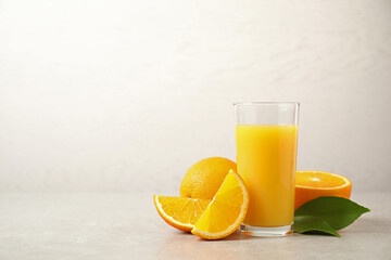 Tasty orange juice, fresh fruits and green leaves on light table. Space for text
