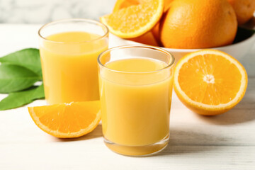 Glasses of orange juice and fresh fruits on white wooden table, closeup