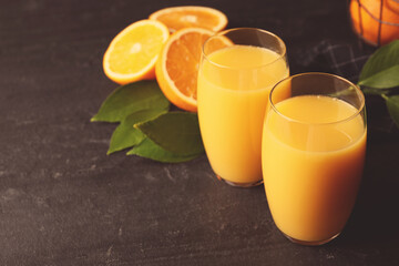 Glasses of orange juice and fresh fruits on black table. Space for text