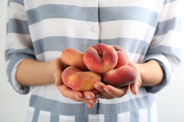 Woman holding heap of fresh ripe donut peaches on light background, closeup