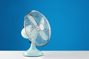 Electric fan on white table against blue background, space for text. Summer heat - obrazy, fototapety, plakaty
