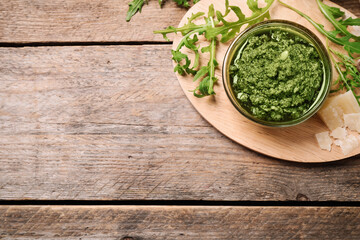 Bowl of tasty arugula pesto and ingredients on wooden table, flat lay. Space for text