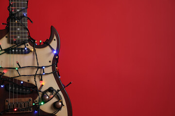 Closeup view of guitar with fairy lights on red background, space for text. Christmas music