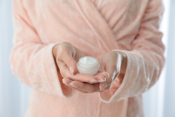Young woman holding jar of cream at home, closeup