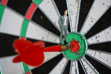 Miniature people: Small business man on red dart arrow hitting in the target center of dartboard....