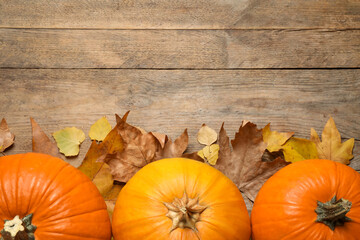 Flat lay composition with pumpkins and autumn leaves on wooden table. Space for text