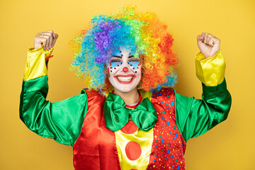 Clown standing over yellow insolated yellow background showing arms muscles smiling proud