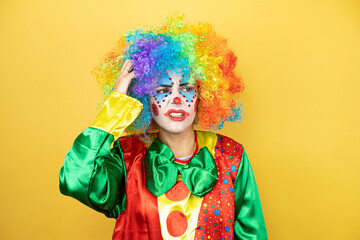 Clown standing over yellow insolated yellow background confuse and wonder about question. Uncertain with doubt, thinking with hand on head