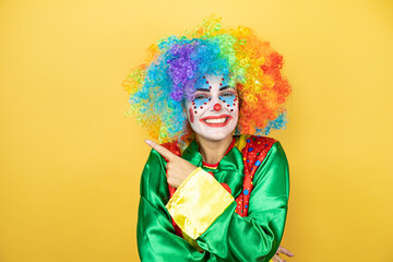 Clown standing over yellow insolated yellow background smiling and pointing with hand and finger to...