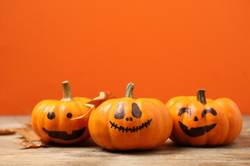 Pumpkins with scary faces and fallen leaves on orange background, space for text. Halloween decor