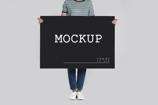 Woman holding black poster with text Mockup Ready To Use on light background, closeup