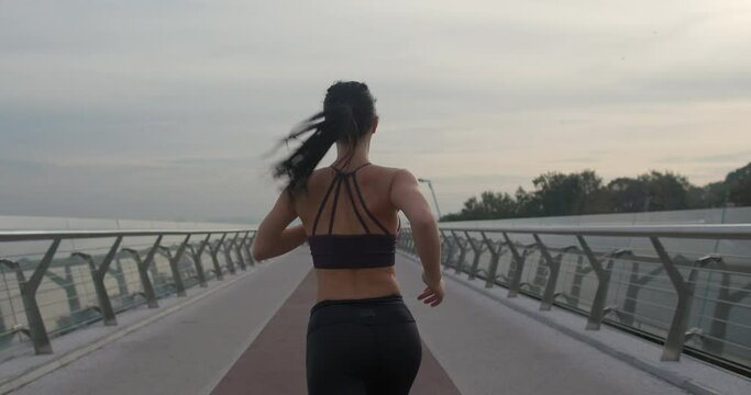Fit female in sportswear running on modern bridge during fitness training in evening in city