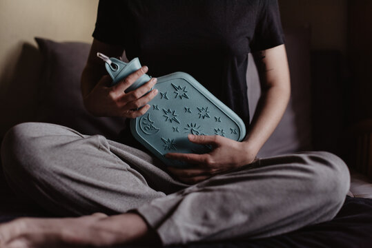 Una mujer sujetando una botella de agua caliente en su est&oacute;mago