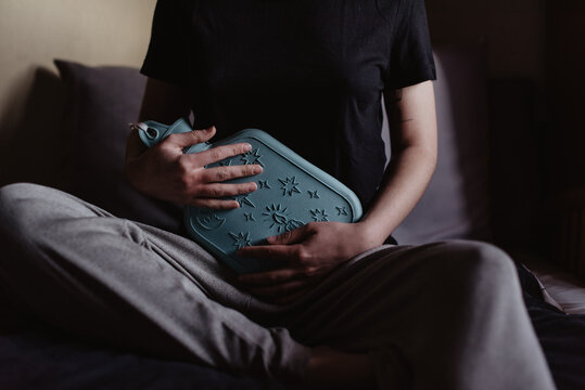 Una mujer sujetando una botella de agua caliente en su est&oacute;mago