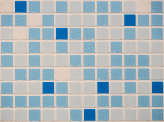 A wall of blue, blue and white small tiles with water droplets on the surface.