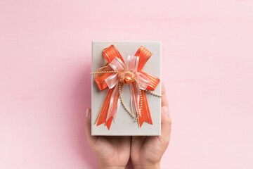 Silver gift box with orange ribbon holding by hand on pink background, present for giving in special day, Top view
