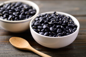 Black kidney beans in a bowl and spoon on wooden background