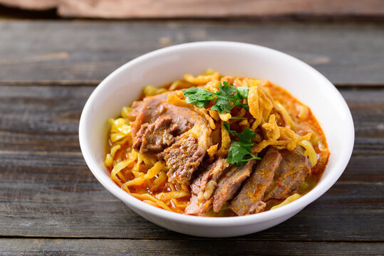 Northern Thai food (Khao Soi), Spicy curry noodles soup with beef in a bowl on wooden background