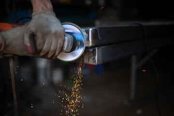 Grinding metal with a grinder. Working in a metal processing workshop. Cleaning the steel seam. The man works with an electric tool. Sparks from metal heating.