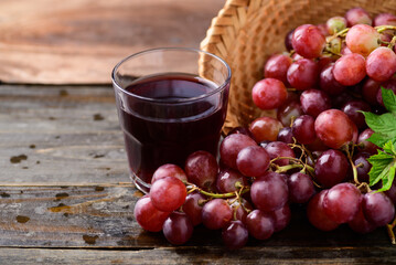 Fresh red grapes fruit in a basket and juice on wooden background