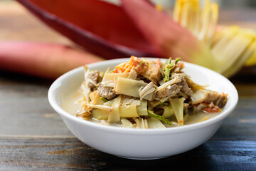 Northern Thai food (Kaeng Hua Plee), banana flower spicy soup with pork in a bowl on wooden table, Local Thai food