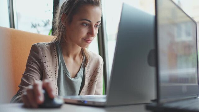 Young smiling business woman working on portable laptop computer. Female copywriter sitting at desk and scrolling mouse, searching, surfing or looking content at laptop