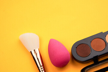 Pink makeup sponge and powder brush yellow background he cropped view
