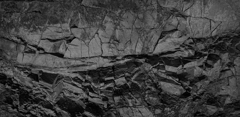 Black and white background. Volumetric black stone background.  Rock texture. Stone wall. Old weathered crumbling surface of a granite mountain. Old weathered crumbling granite mountain.