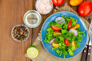 Light meal of green leaves of lettuce, yellow and red tomatoes, olive oil on wooden table.