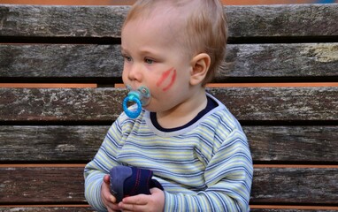  boy with a pacifier in his mouth sits on a bench and holds shoes in his hand