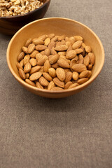 Almonds in wooden bowl on brown background.