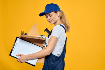 Woman with a box of construction tools and in a cap on a yellow background repair construction industry