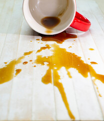 A picture of a coffee drink spilled out of a red glass on a white wood floor