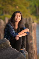 Young woman or teen sitting along lake pier at sunset