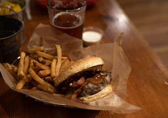 Closeup of a bacon cheeseburger, fries, and a beer inside a restaurant. (Soft background focus)