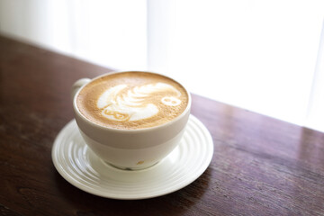 A cup of hot latte art coffee on wooden table.