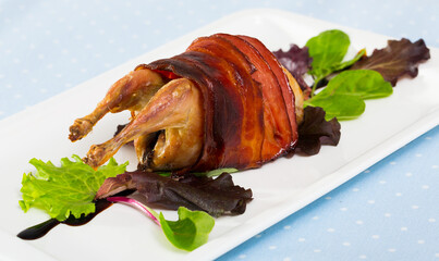 Image of baked in bacon quail with balsamic sauce on the plate indoors.