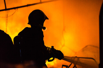 Silhouettes of strong and brave firefighter using water and extinguisher to fighting with fire flame in an emergency situation.