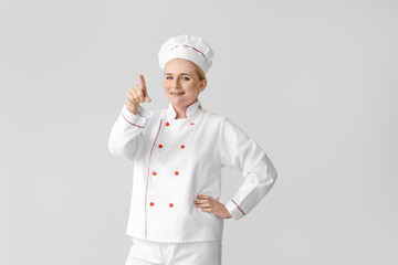 Mature female chef pointing at something on grey background