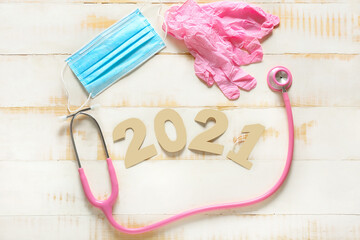 Stethoscope, medical mask, gloves and figure 2021 on wooden background
