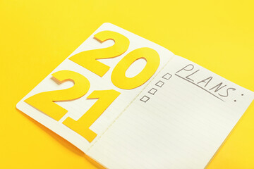 Notebook with word PLANS and figure 2021 on color background