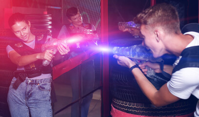 Obraz premium Group portrait of jolly emotional people with laser guns playing laser tag game together in dark labyrinth
