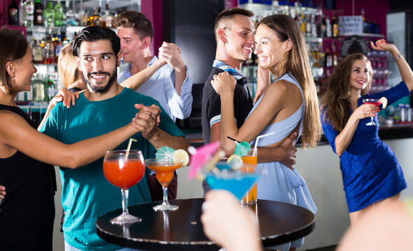 positive women with men dance in pairs on the dance floor in a nightclub