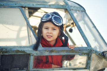 Portrait of a cute little girl in the cockpit of an old plane. Childhood dreams of aviation.
