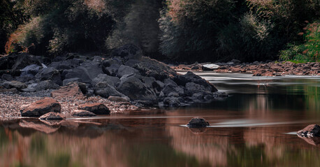 Long exposure reflected of rocks and trees on the river in autumn.