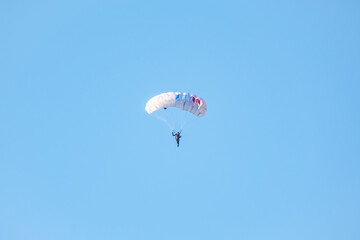 one parachutist floats slowly at low altitude on the background of clear sky
