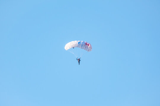 one parachutist floats slowly at low altitude on the background of clear sky